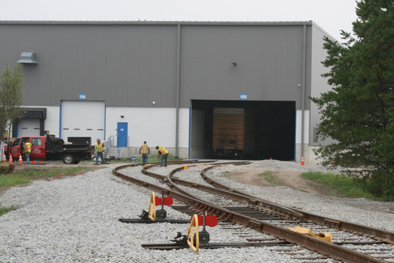 FIGURE 3. Two-Track Siding Inside Expanded Warehouse
This image shows two railroad tracks entering a modern warehouse. There is a large boxcar positioned on one track for indoor loading and unloading.
